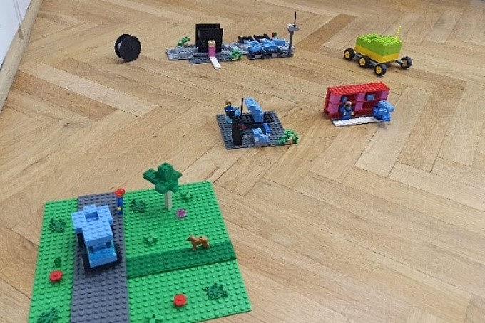 Various vehicles and buildings made of colorful Lego bricks are spread out on a parquet floor.