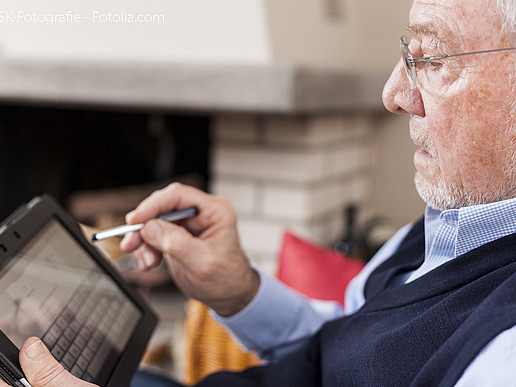 Elderly man using a stylus on a tablet.