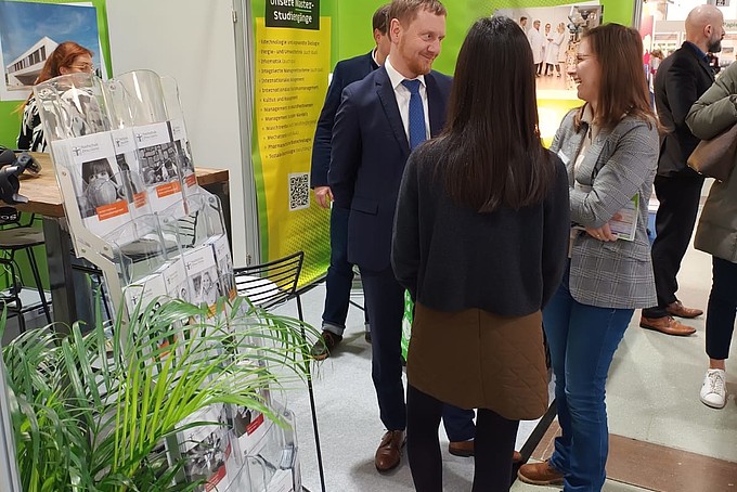 Minister President Kretschmer, the HSZG student advisor and Zhaniya talk at the stand.