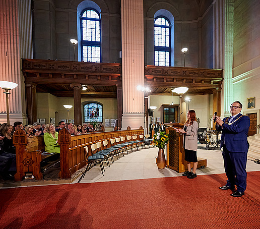 Rektor und Moderator stehen am Altar und schauen ins Publikum.