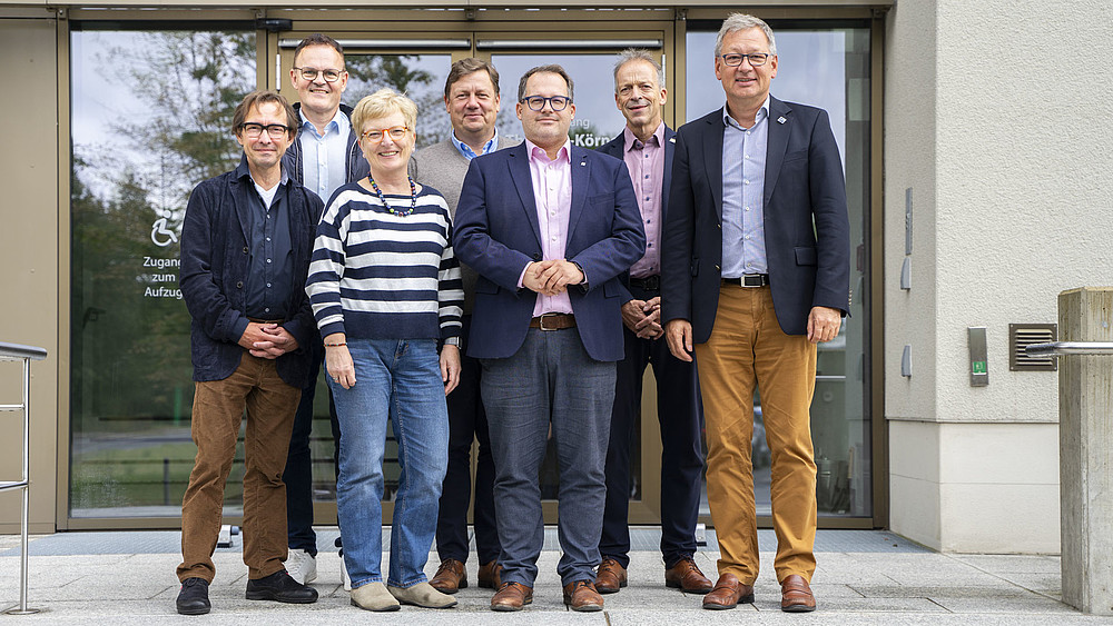 The university rector and the rectors stand on the stairs in front of building one for the group photo and smile into the camera.