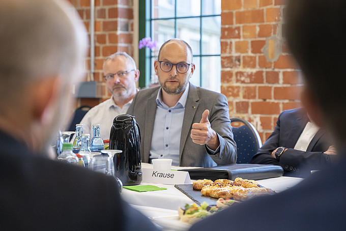 A man with glasses talks and gesticulates during a meeting at the table, other participants listen and look at him.