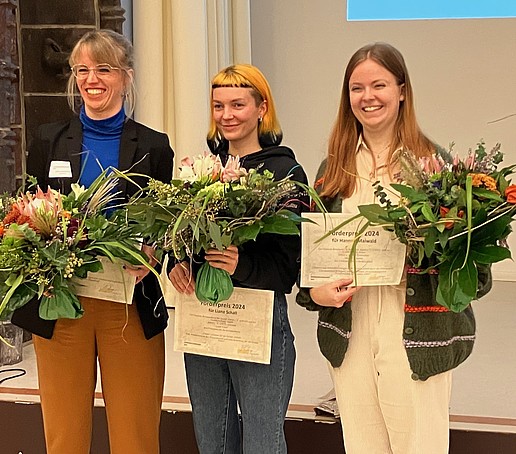 Drei Preisträgerinnen stehen mit Urkunden und Blumensträußen nebeneinander.