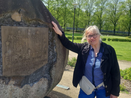 Mrs. Schönfelder is standing in a park and leaning against a large stone.