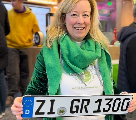 The vice principal holds the Sprinter license plate in her hands and stands in front of the open AirStream trailer.