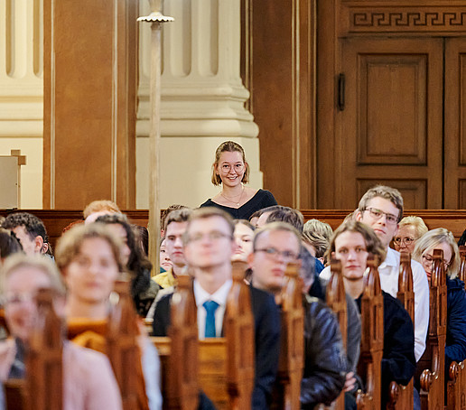 Aus einer vollen Sitzreihe steht eine Studentin auf.