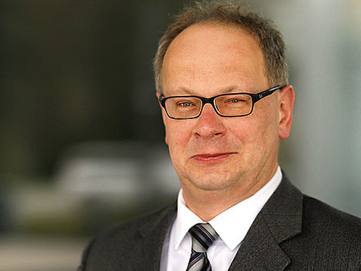 Prof. Meißner wears glasses and a suit and tie. He smiles into the camera.
