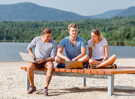 Two students and a female student on a bench on the beach at Lake Olbersdorf.