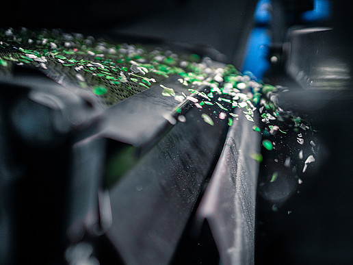 Grüne Kunststoff-Flakes fliegen aus einer Maschine.