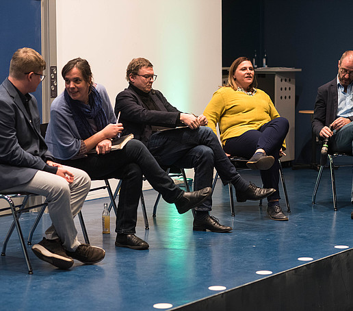 5 Menschen sitzen auf Stühlen auf einer Bühne.