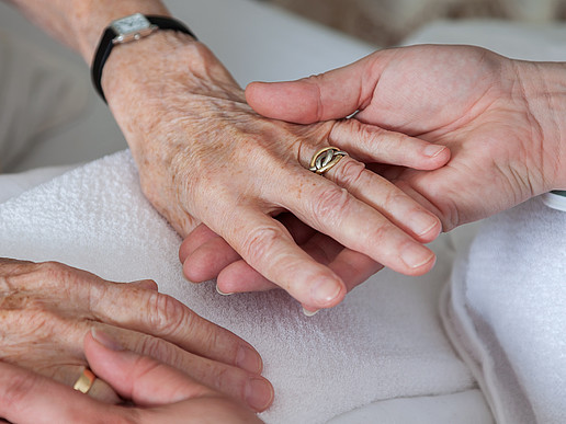 Two hands of a clearly older person hold the hands of a younger person.