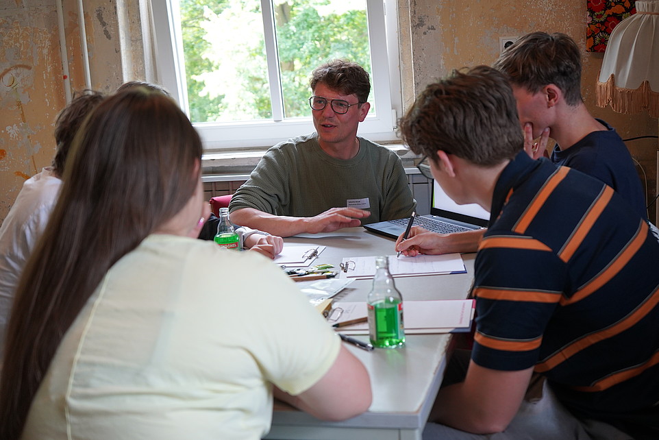 Sebastian Benad sits at a table and discusses with a group of young people in a workshop.