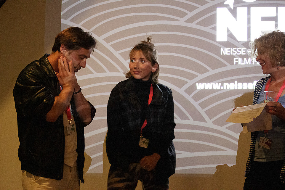 Festival organizers talk in front of a wall with an NFF projection.