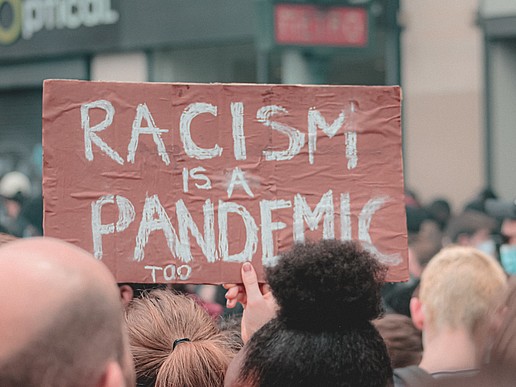 Demonstrators against everyday racism hold up a sign reading "Racism is also a pandemic".