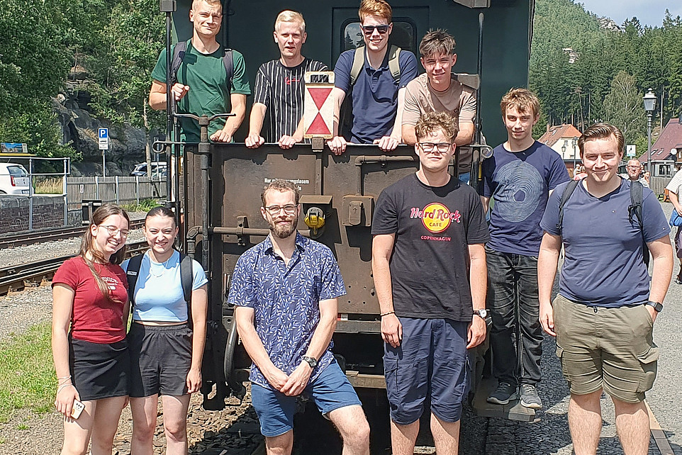 Am Ende des Eisenbahnwagons der Bimmelbahn posieren die Teilnehmenden für ein Gruppenfoto.