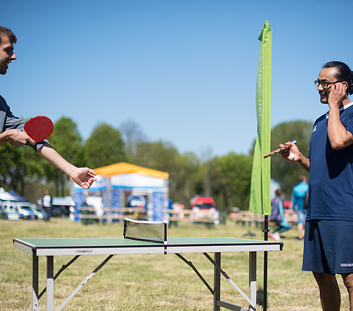 Two players play table tennis in front of the tent.