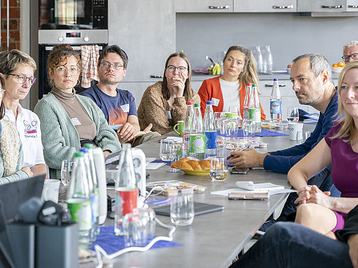 Hochschulmitarbeitende und Gäste sitzen im Celsiuz an einem langen Tisch und lauschen einem Vortrag.