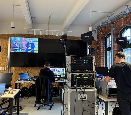 Employees sit and stand in a technical and production room, surrounded by production technology.