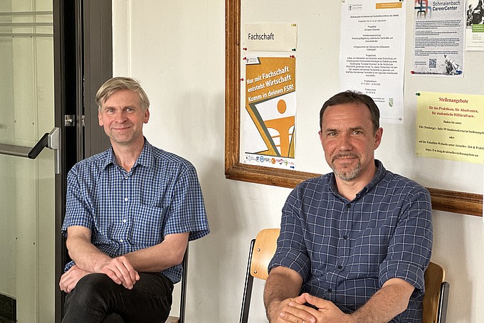 Mr. Zücker and Mr. Fallgatter are sitting on chairs, a pinboard can be seen in the background.