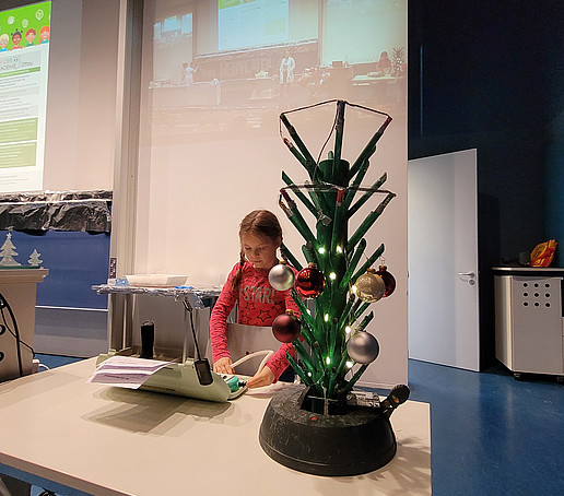 A girl plays the melodica, in the foreground there are table fireworks in the shape of a Christmas tree.