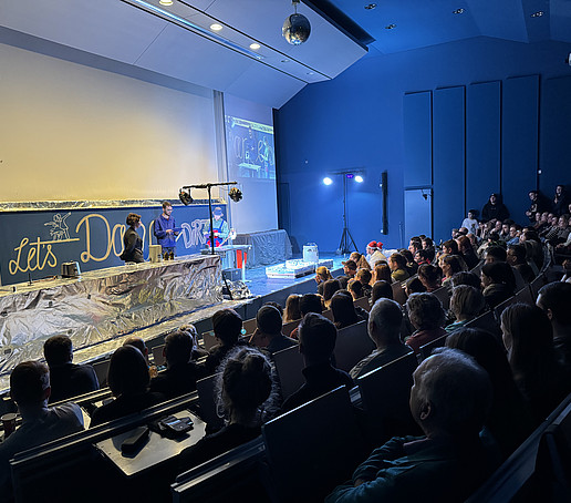 Vollbesetzte Reihen im Audimax. Auf dem Podium sind aufwändige Versuchsvorrichtungen aufgebaut.