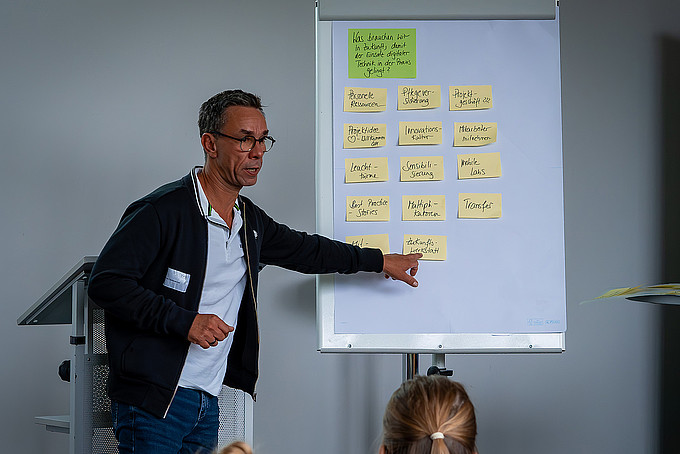 A speaker points to a flipchart.