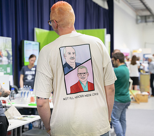 Ein Mitarbeiter mit T-Shirt, auf dem zwei Comic-Zeichnungen von zwei Professoren zu sehen sind.