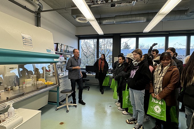 Prof. Dr. Thomas Wiegert stands in a laboratory at the HSZG and speaks to a group of international prospective students at the Rahn Studienkolleg Leipzig. The participants stand in a group and listen attentively. Laboratory equipment and work materials can be seen in the background.