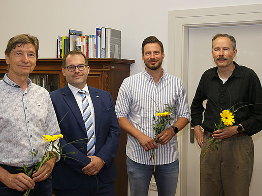The Rector and three HSZG employees stand in the Rector's office and smile at the camera. The employees are holding a flower in their hands to thank them for their secondment to the health authorities in Bautzen and Görlitz.