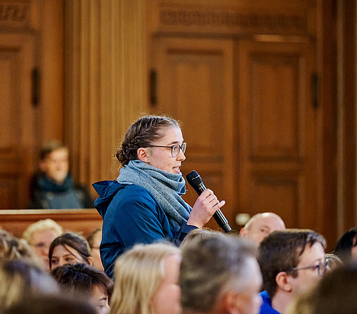 Eine Studentin steht und spricht ins Mikro.