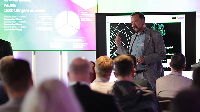 David Sauer gives a presentation on a digital screen in front of an audience.