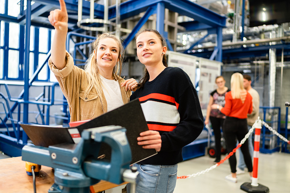 Two students are standing in the Zittau power plant laboratory. Their eyes fall in the direction one of the students is pointing.