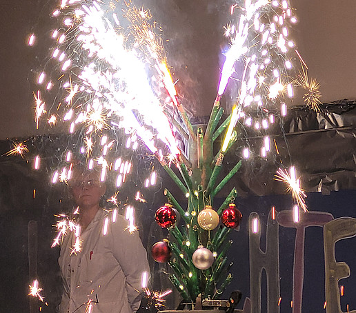 A table firework in the shape of a Christmas tree burns on a table on the stage.