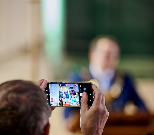 The rector can be seen at the lectern on a raised cell phone display.