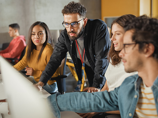 Eine Gruppe Studierender unterhält sich und zeigt dabei auf einen Laptop.