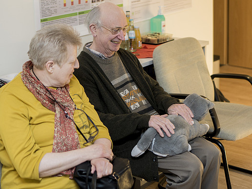 Elderly couple has a stuffed cat on their lap and laughs.